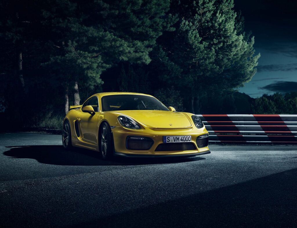 Striking Yellow Porsche Cayman: Sleek Design Against Dramatic Background Wallpaper
