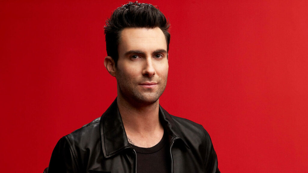Stylish young Adam Levine in leather jacket on solid red background, exuding confidence. Wallpaper