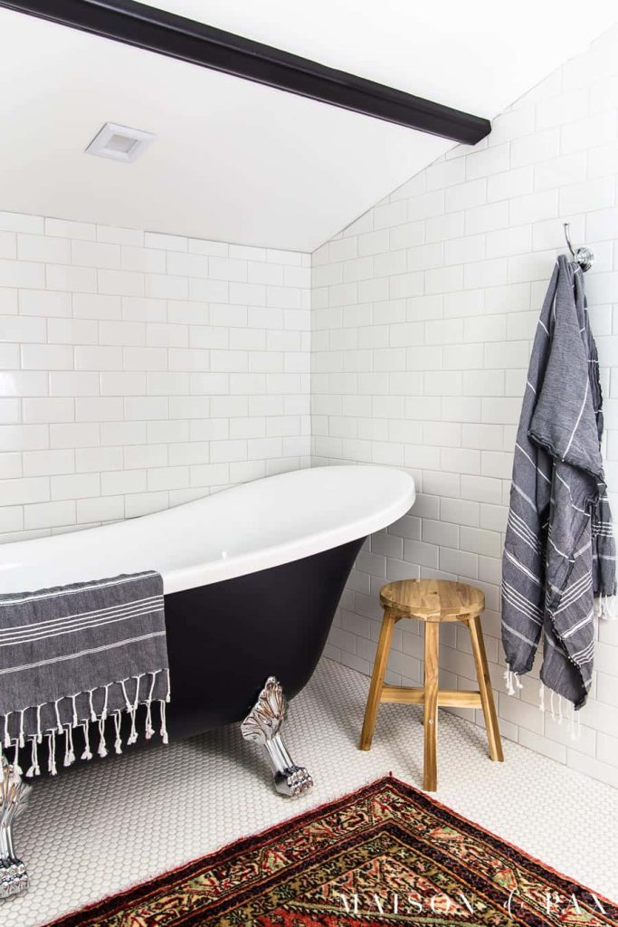 Elegant black and white bathroom with clawfoot tub white subway tiles patterned rug and wooden stool Wallpaper