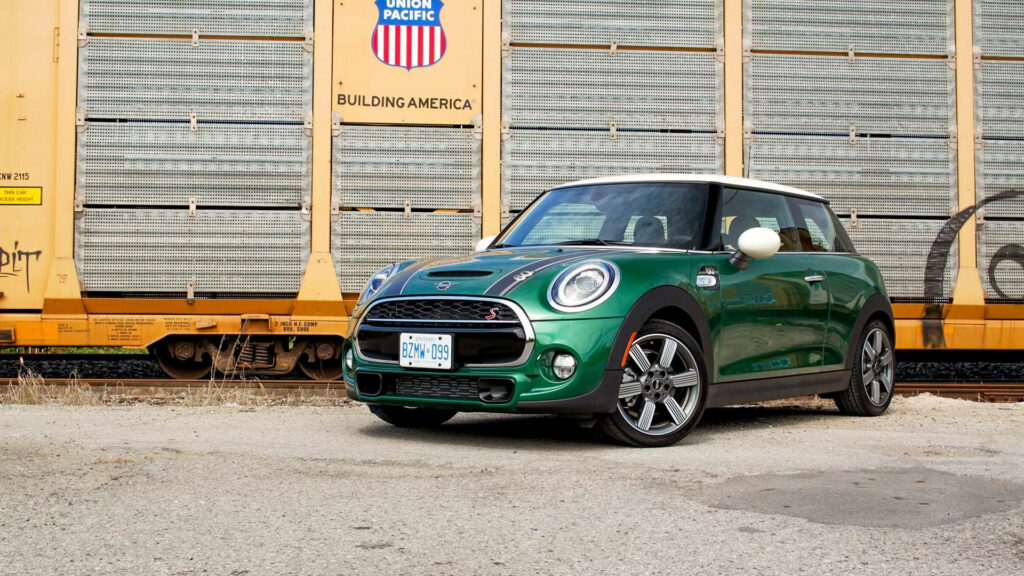 Green Mini Cooper parked on sunlit pavement outside gold building urban modern wallpaper background