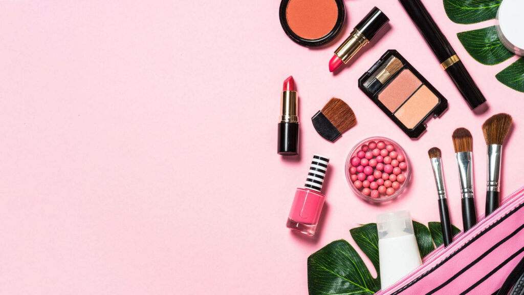 Makeup essentials wallpaper with lipstick blush brushes eyeshadow on pink background with green leaves