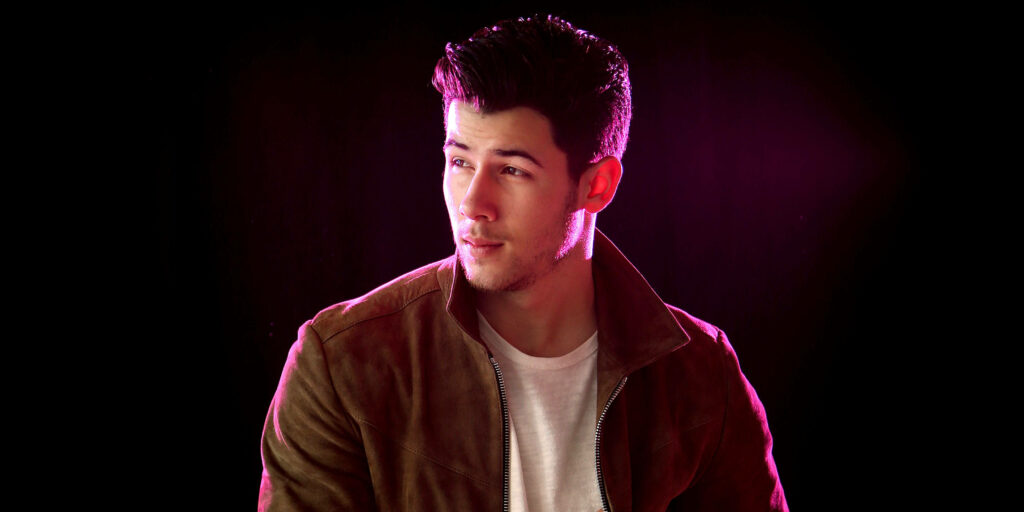 Stylish Wallpaper of Nick Jonas in Brown Jacket against Dark Background