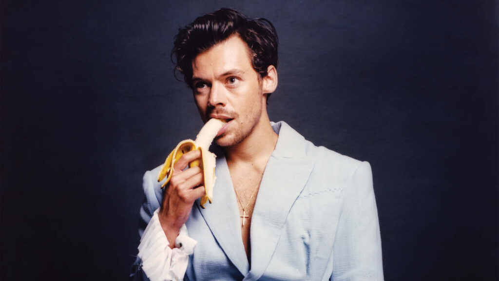 Charming British Crooner Harry Styles Casually Snacking on a Banana in Scenic Surroundings Wallpaper