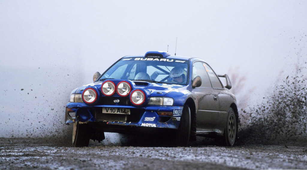 Classic Subaru rally car speeding through muddy offroad track showcasing intense motorsport action Wallpaper
