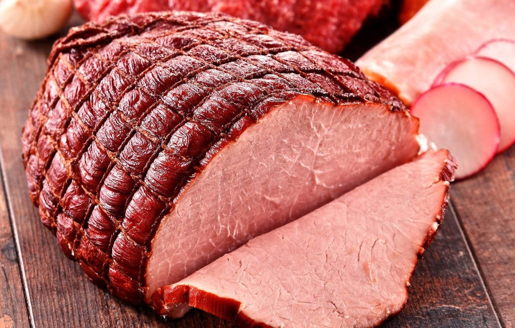 Glazed diamond scored baked ham slice on wooden board with radishes warm lighting background Wallpaper