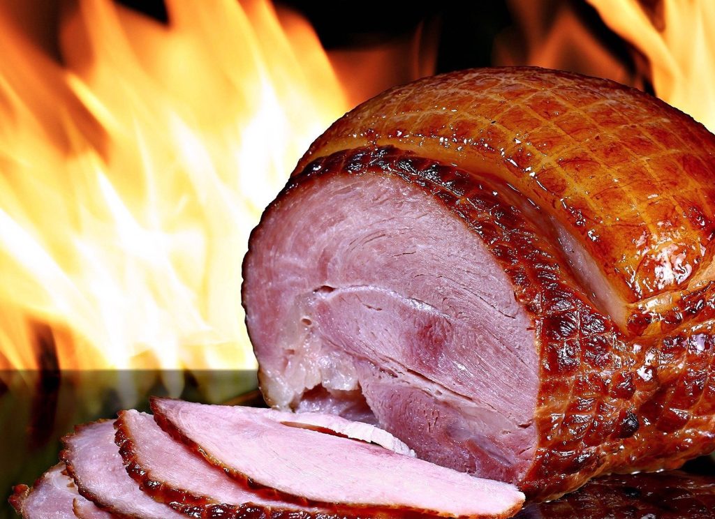 Glazed cured ham with golden crust sliced against vibrant orange and yellow flame background wallpaper