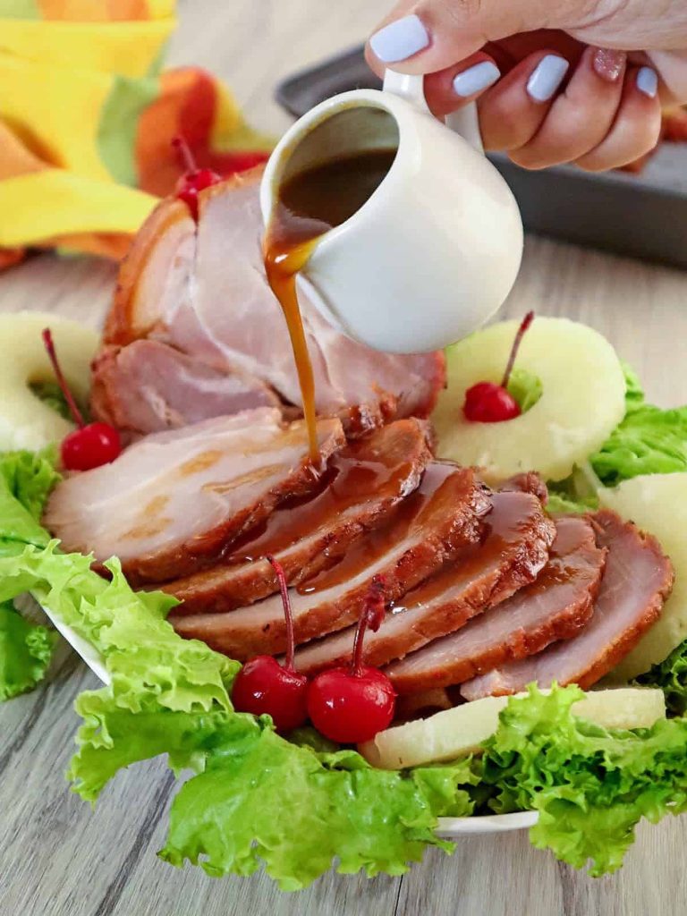 Glazed sliced ham with pineapple rings and cherries on lettuce being drizzled for holiday meal Wallpaper
