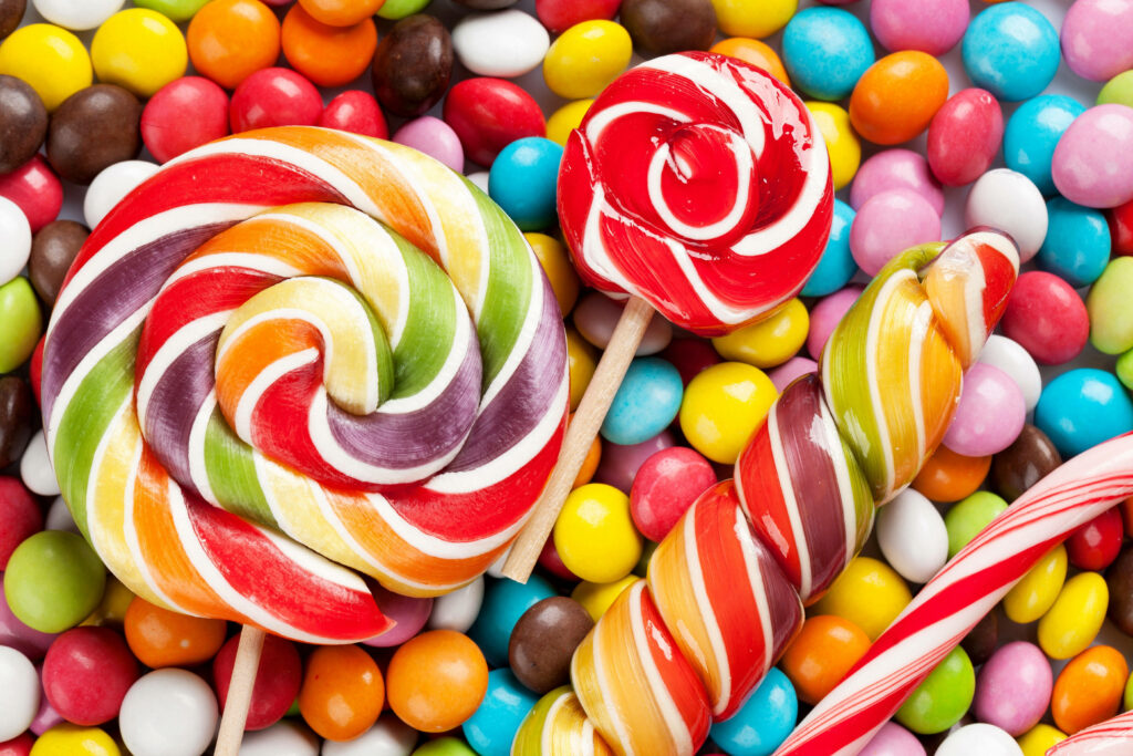 Sugar Landscapes: Magnificent Rainbow Spiral Lollipop and Shiny Round Candies on Candy-Coated Backdrop Wallpaper