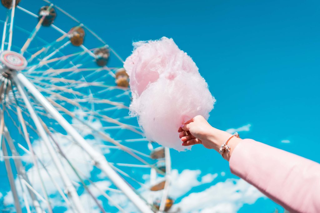 Hand holding pink cotton candy with Ferris wheel and bright blue summer sky background Wallpaper