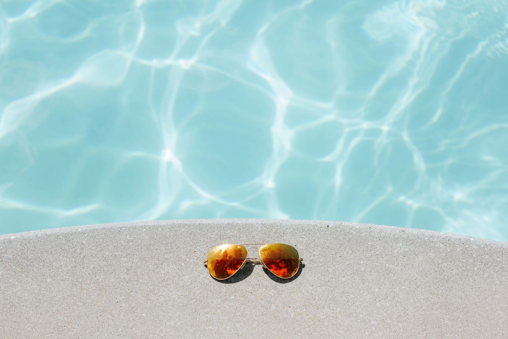 Aviator sunglasses on ledge by turquoise pool in bright sunlight for summer relaxation wallpaper