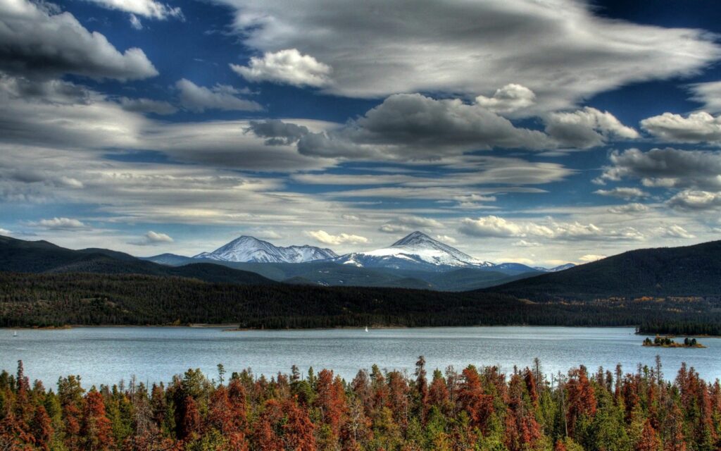 Peaceful river with lush trees snow-capped mountains and dramatic clouds summer landscape wallpaper