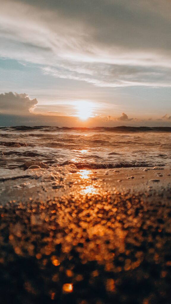 Summer sunset over sea with golden light reflecting on waves and wet sand serene coastal view Wallpaper