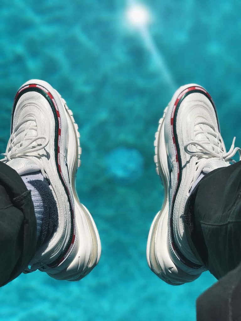POV shot of Nike Air Max 97 Undefeated sneakers by a shimmering blue pool summer streetwear wallpaper
