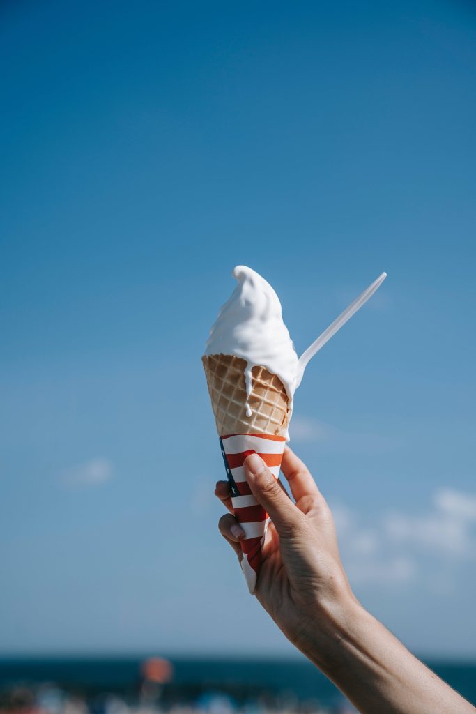 Hand holding white soft serve ice cream with American flag wrapper against blue sky wallpaper