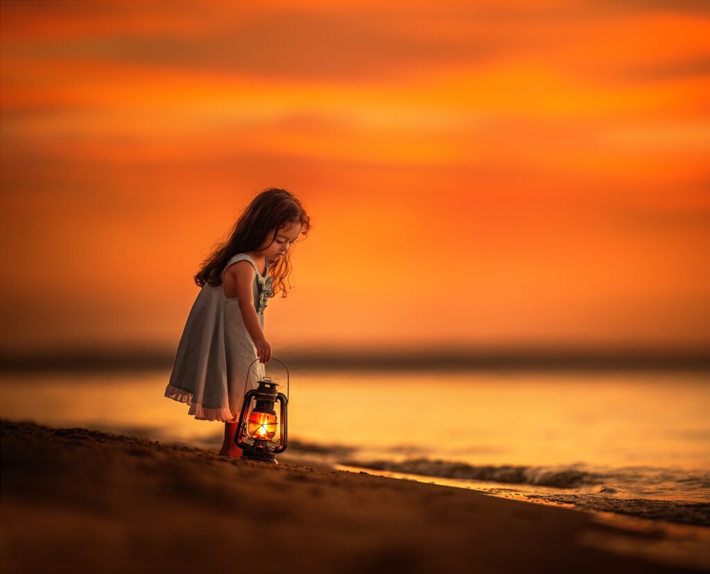 Radiant Twilight: A Little Girl's Dreamy Moment by the Beach with Her Cute Lantern Wallpaper