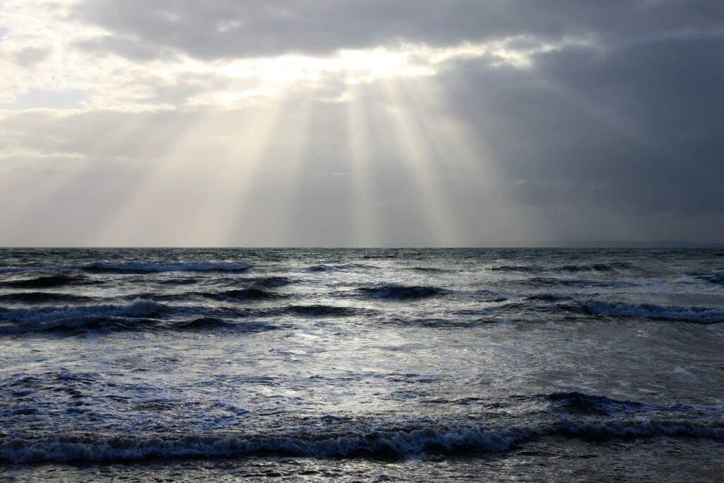 Sunbeams piercing dramatic clouds over serene ocean waves with moody sky scenic seascape wallpaper
