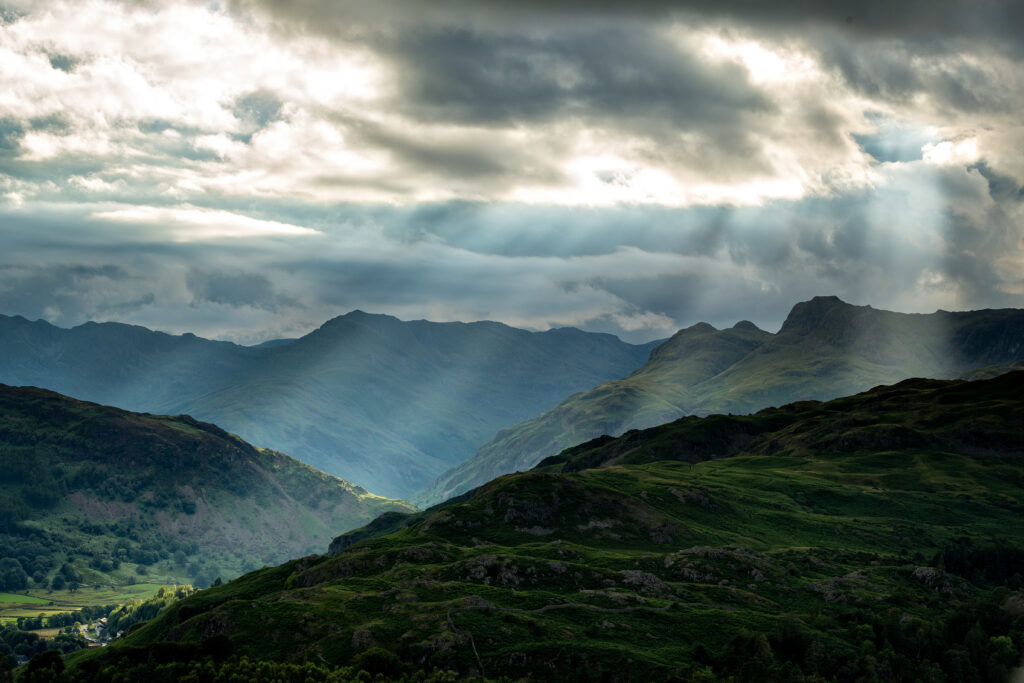Sunbeams shining through clouds over rugged mountains and lush green landscape wallpaper background