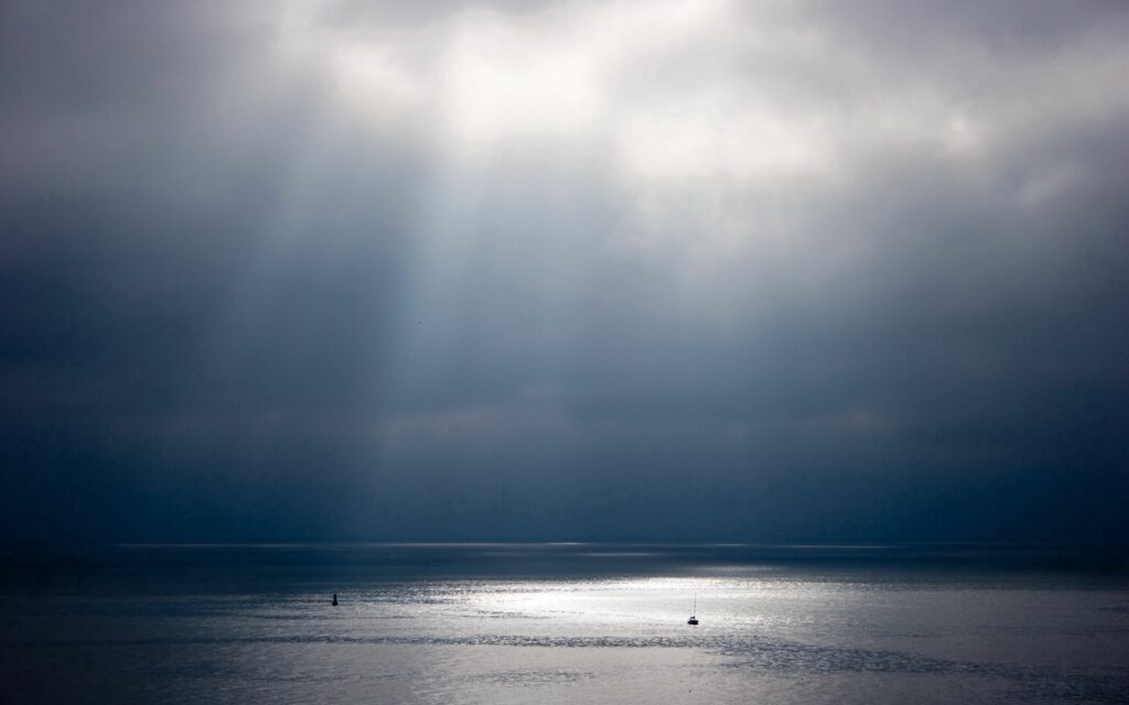 Sunbeams piercing moody sky lighting calm water with shimmering rays and peaceful reflections Wallpaper