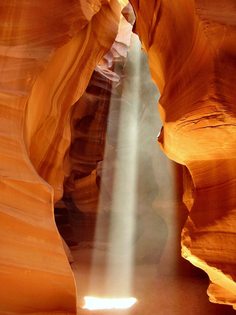 Sunlight beam illuminates warm textured sandstone walls in narrow Antelope Canyon background Wallpaper