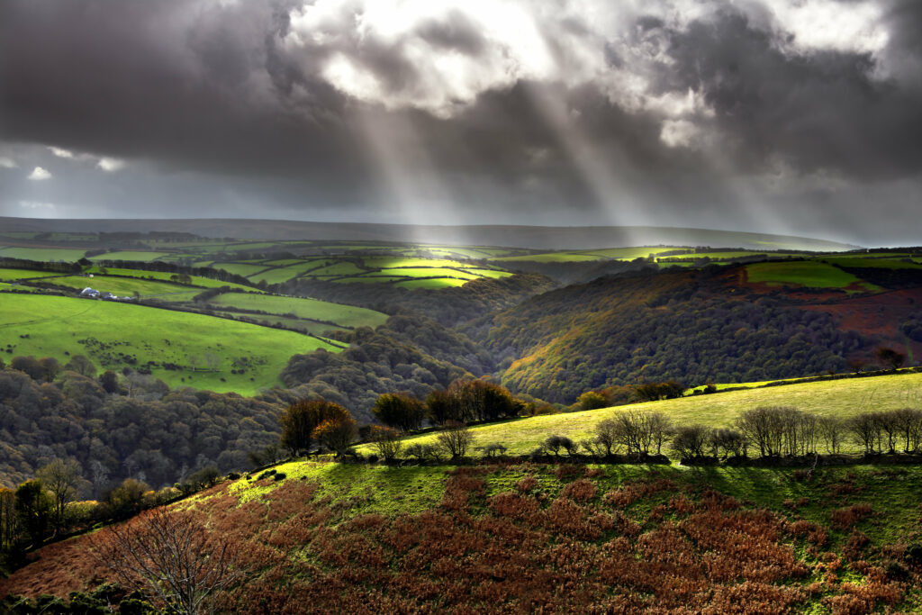 Sunlight through dramatic clouds lighting vibrant green hills and lush countryside fields wallpaper