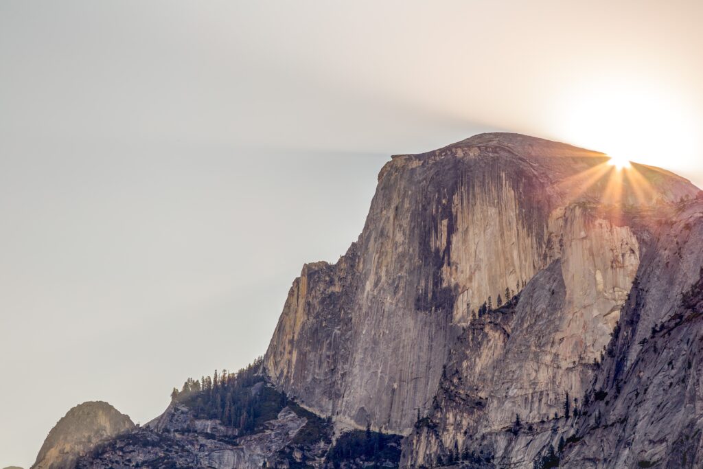 Sunlight lighting rugged mountain cliff face with soft shadows against a calm sky wallpaper background
