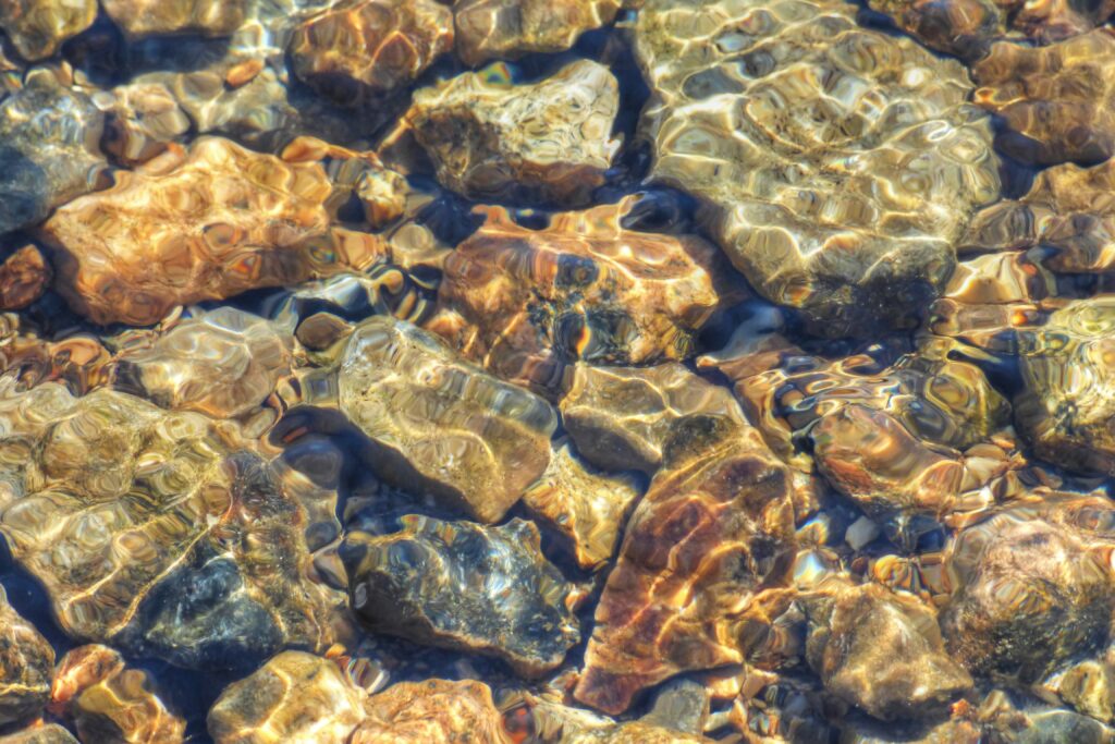 Sunlight shimmering over stones beneath clear flowing water with rippling natural patterns wallpaper