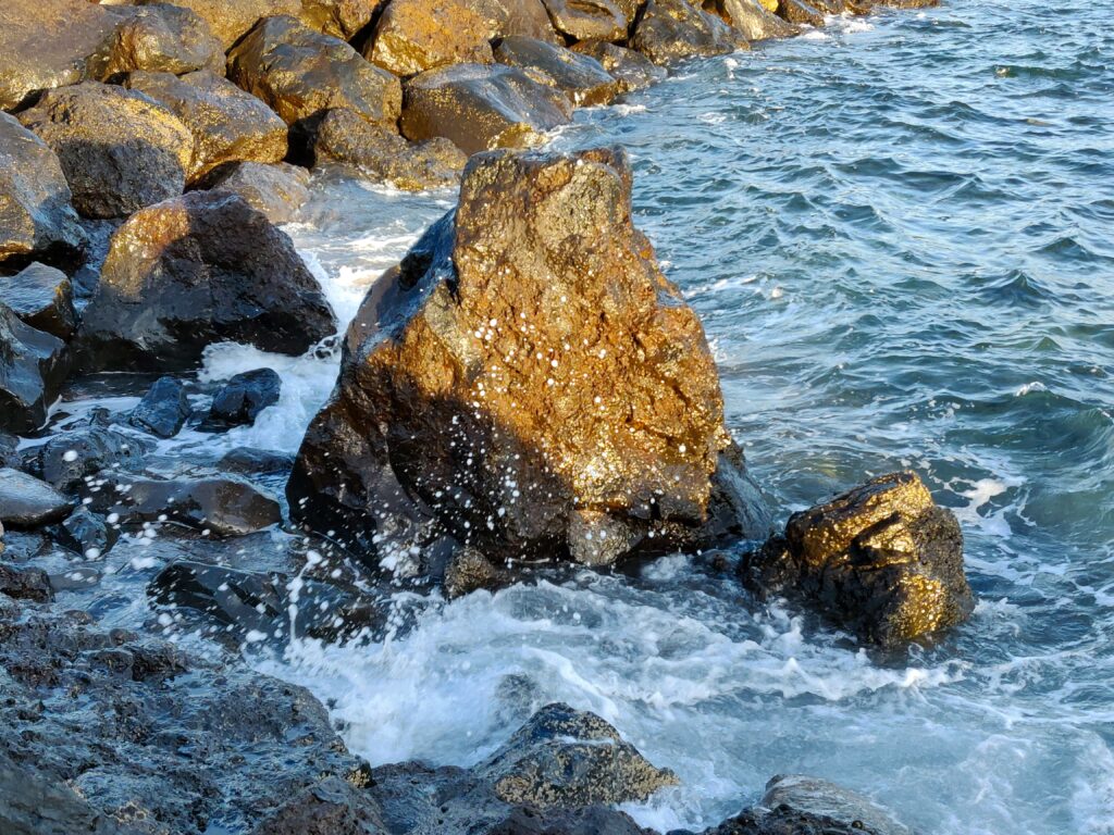 Sunlight on rugged rocks with ocean waves crashing and foamy splashes vivid shoreline energy Wallpaper