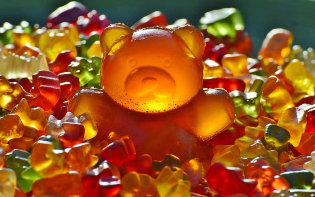 Macro photo of sunlit amber gummy bear on colorful translucent candies glossy texture wallpaper