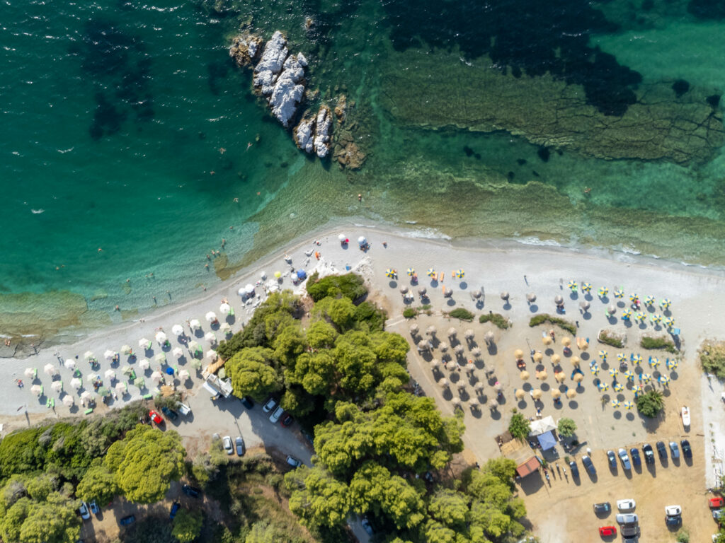 Aerial view of sunlit beach resort with umbrellas lounge chairs turquoise sea and lush greenery Wallpaper