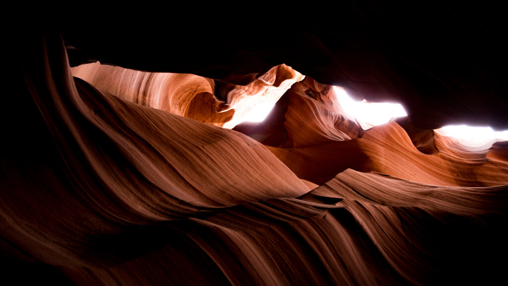 Sunlit canyon cave with textured sandstone layers showcasing dramatic curves and patterns Wallpaper