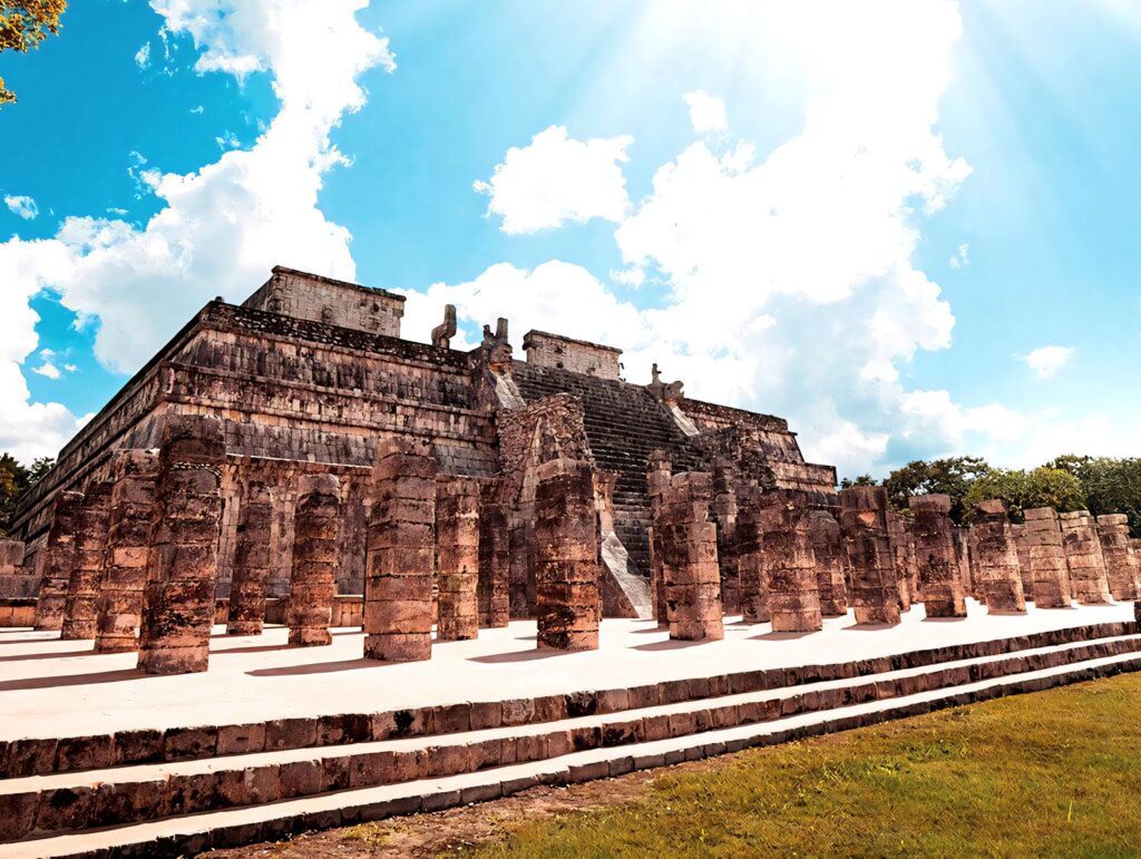 Sunlit Chichen Itza Mayan pyramid and stone columns under blue sky with white clouds wallpaper background