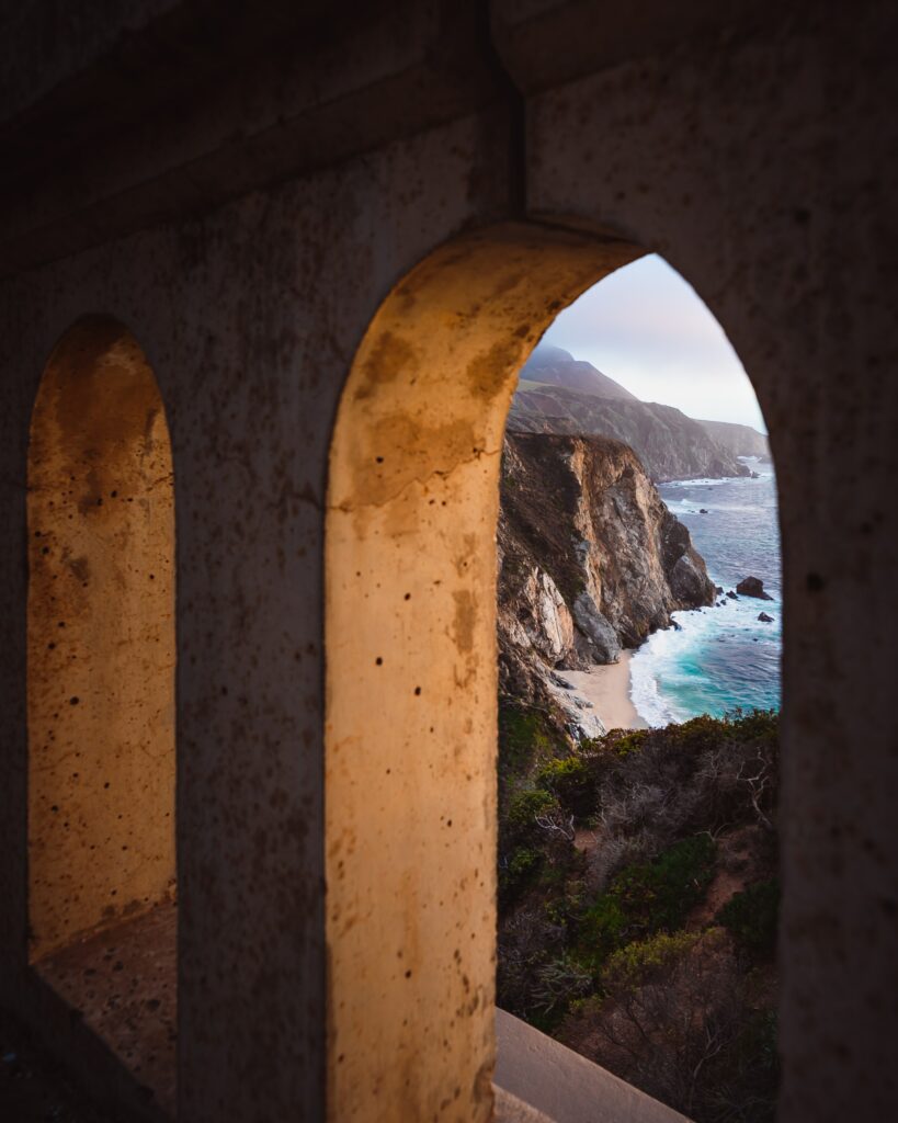 Weathered stone arches framing rugged cliffs and calm blue sea with warm sunlight coastal view Wallpaper
