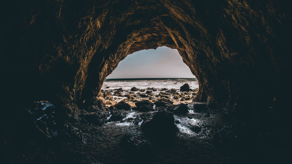 View from rocky cave interior looking out at sunlit sea surf and reflective coastal stones wallpaper
