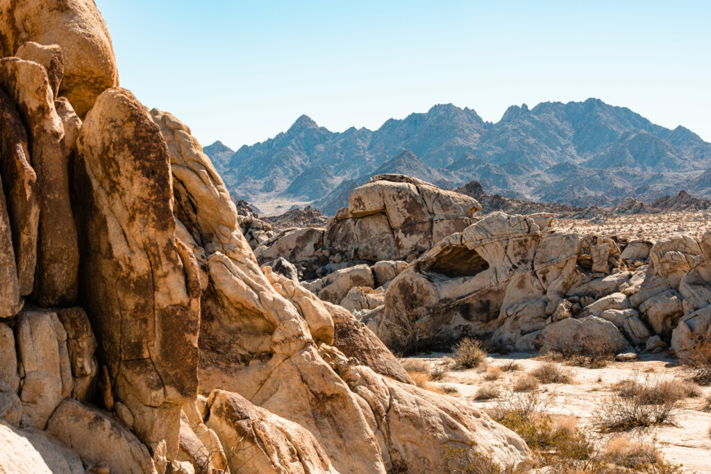 Sunlit desert landscape with rugged rock formations weathered stones and distant mountains Wallpaper