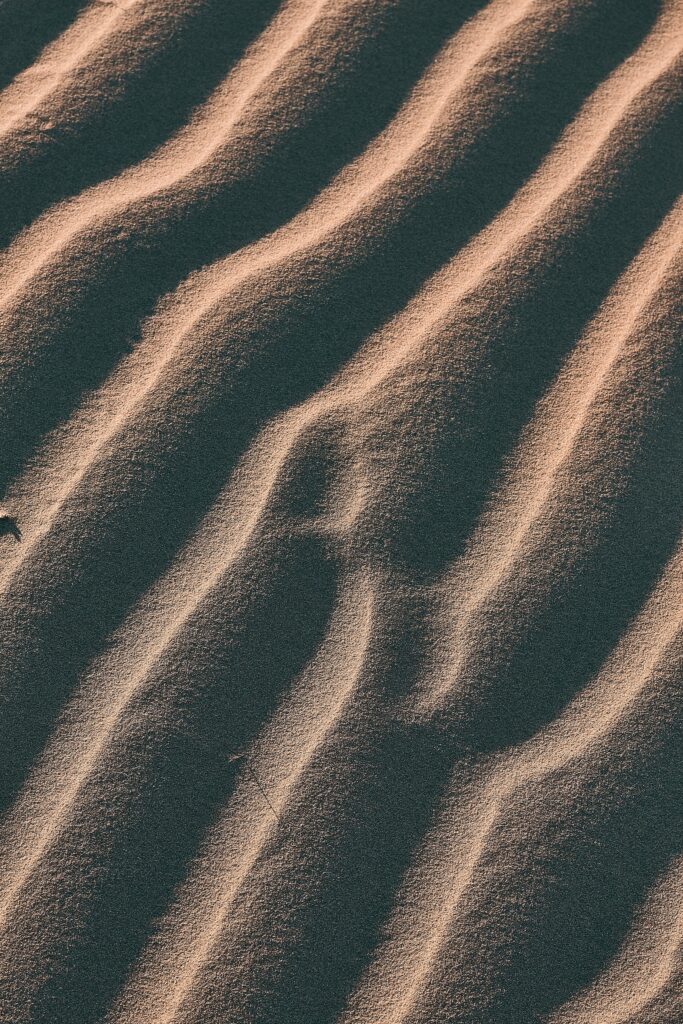 Close-up of desert sand dunes with wavy patterns and warm sunlight highlighting textured surface Wallpaper
