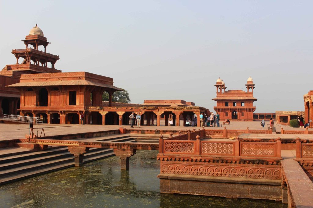 Sunlit red sandstone Panch Mahal and Anup Talao pool at historic Fatehpur Sikri Fort with tourists Wallpaper