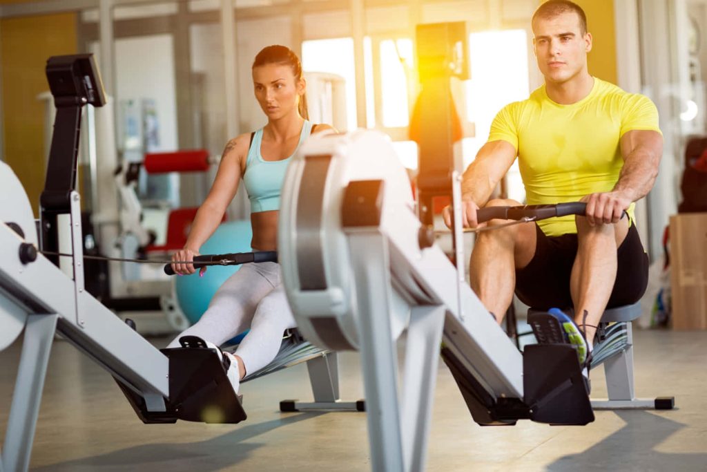 Fit man and woman rowing in sunlit gym fitness wallpaper motivational workout background
