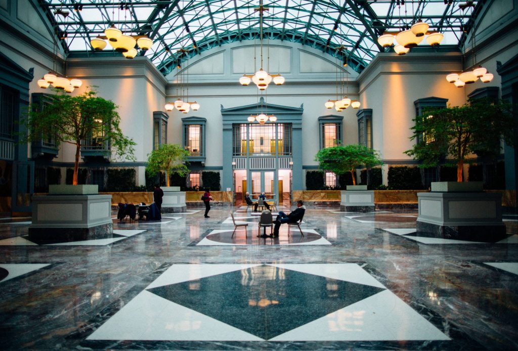 Sunlit hotel lobby wallpaper with glass ceiling geometric marble floors and indoor trees