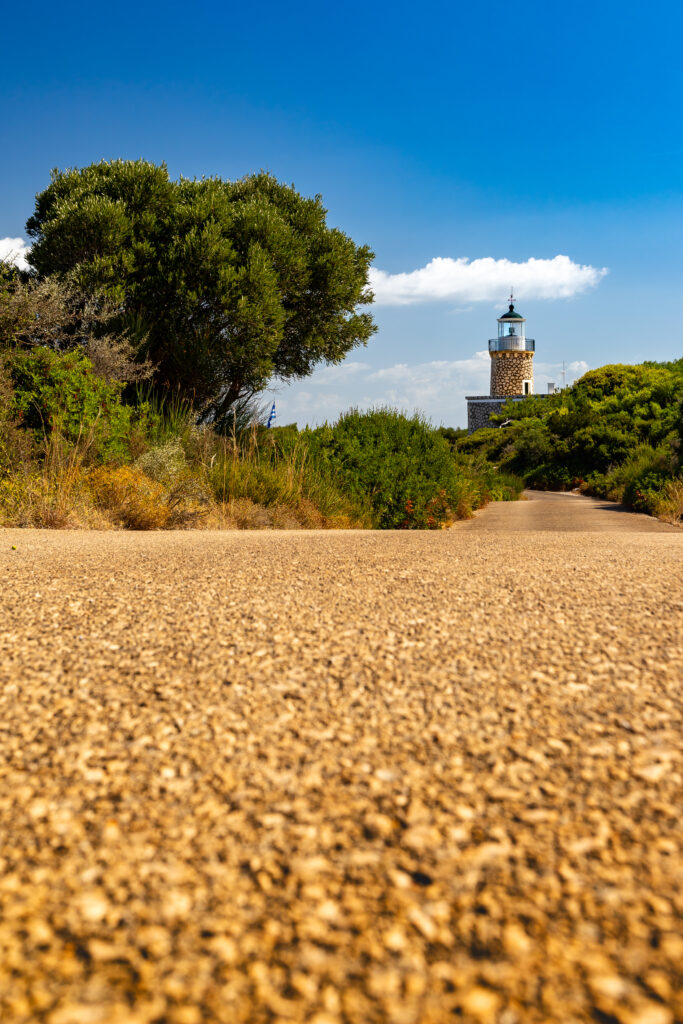 Lighthouse tower behind green trees under clear blue sky with blurred textured path foreground Wallpaper