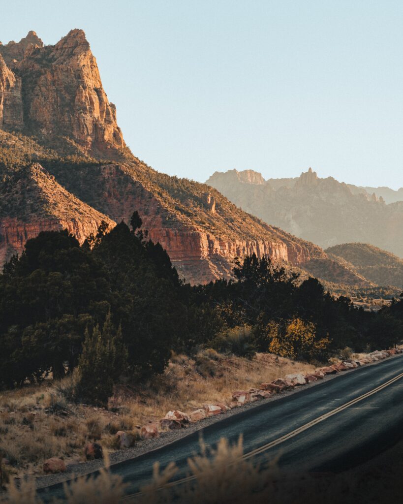 Scenic mountain landscape with rugged peaks warm sunlight winding road and dense trees background Wallpaper
