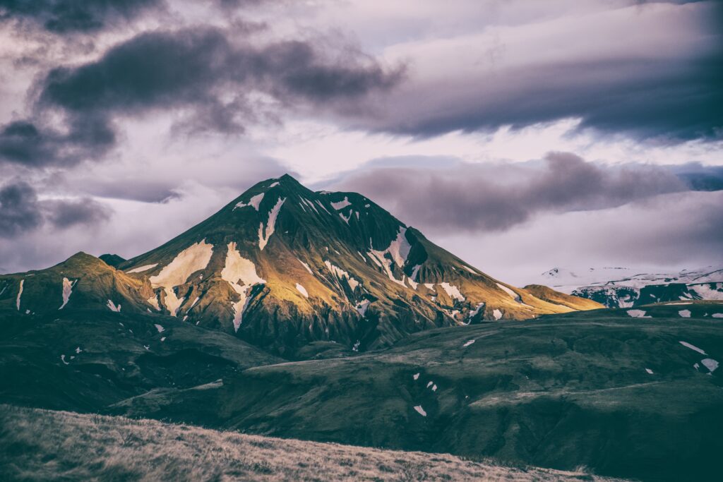 Sunlit mountain summit with snow patches and dramatic clouds for nature wallpaper background