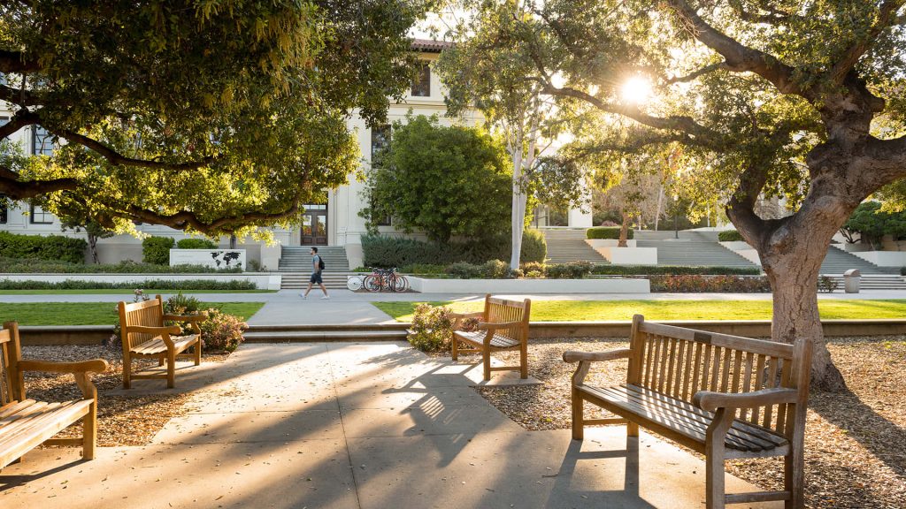 Sunlit Occidental College campus quad with trees benches and classic architecture background Wallpaper