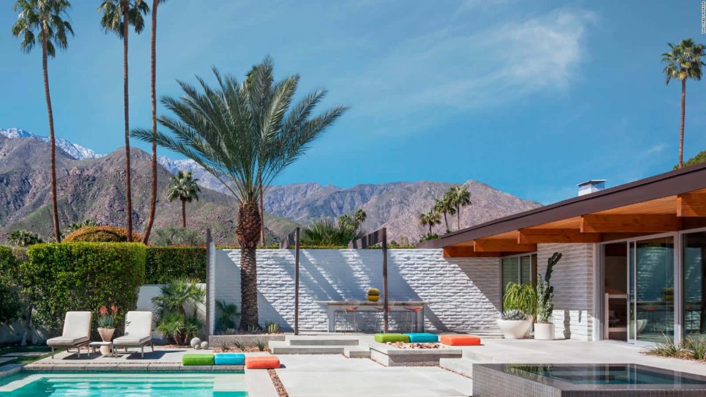 Sunlit Palm Springs mid-century patio with turquoise pool vibrant cushions and snowy mountains Wallpaper