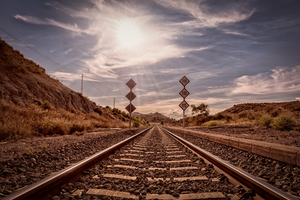 Low angle railroad scene with sunlit rails and rocky landscape under streaked cloudy sky wallpaper