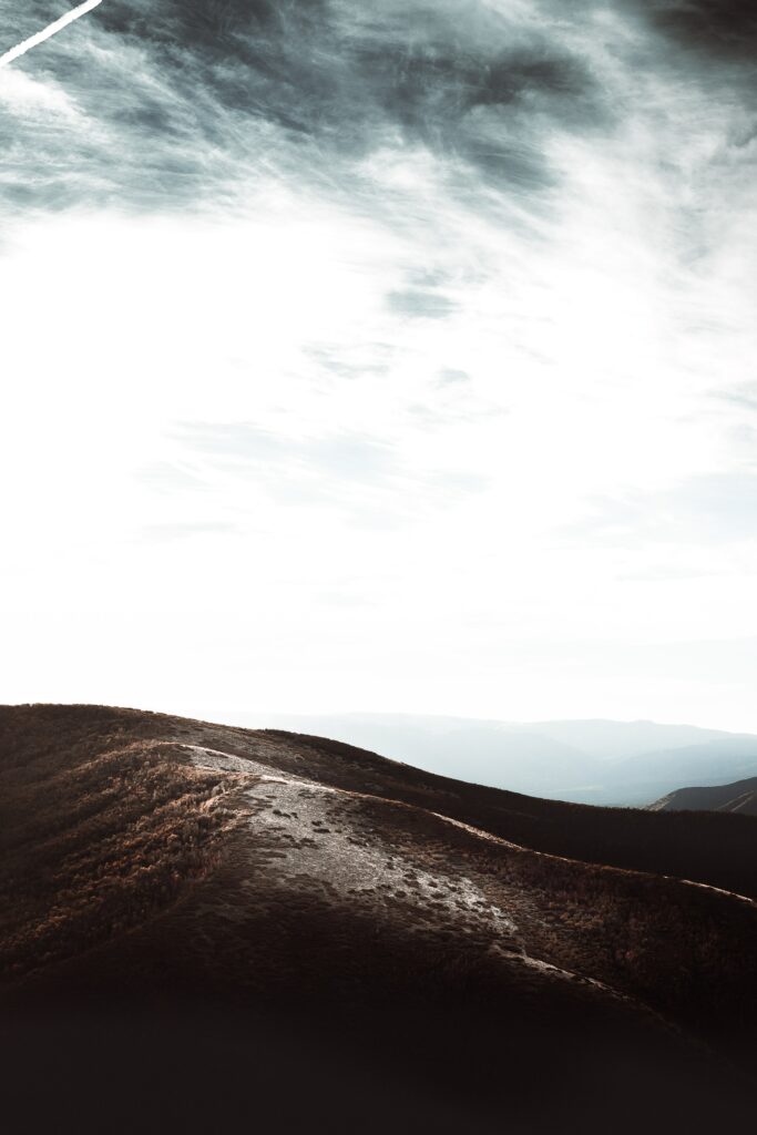 Sunlit rolling hills and misty mountains under cloudy sky serene natural landscape wallpaper