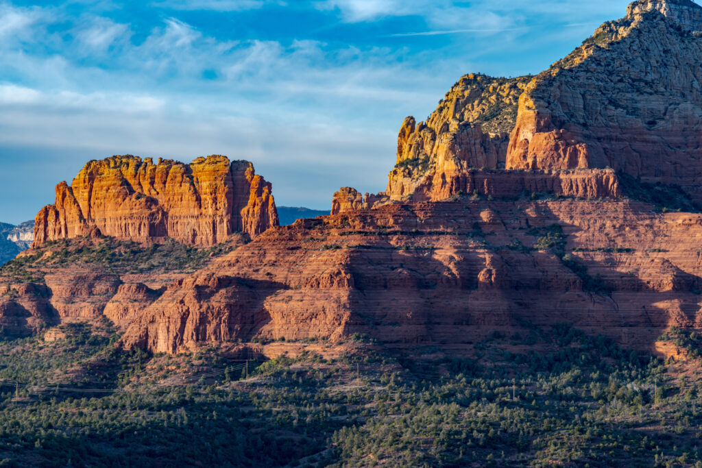 Rugged mountains and rock formations bathed in warm sunlight with green vegetation and blue sky Wallpaper