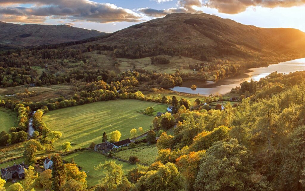 Sunlit aerial view of Scotland mountains river green fields and trees at warm sunset wallpaper background