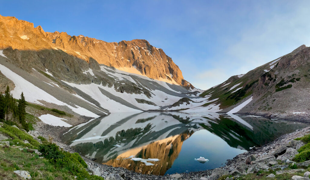 Snow-capped mountains reflected in alpine lake with sunlight lush greenery and rocky terrain wallpaper