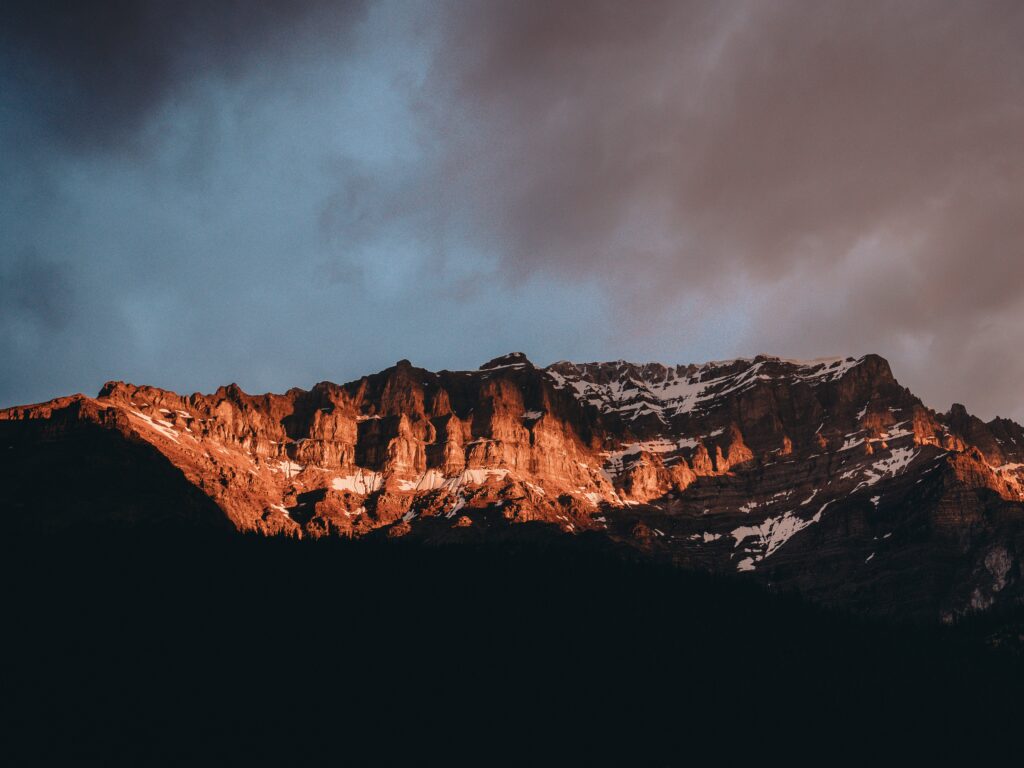 Sunlit snowy rocky mountain peaks under dramatic sky showcasing Canadas rugged landscape wallpaper