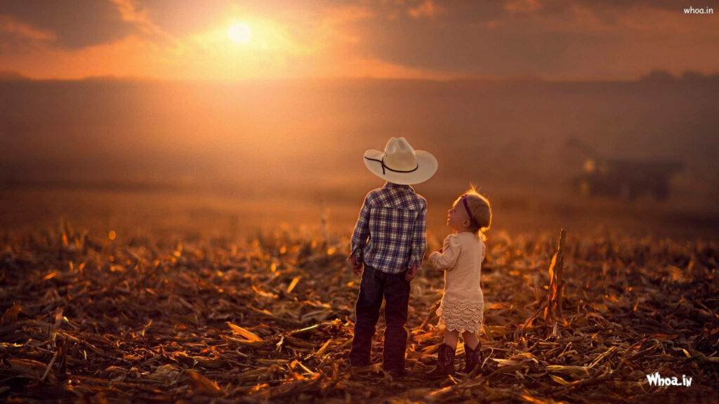 Two children in a sunlit field at sunset one dressed as cowboy sharing a moment of friendship Wallpaper